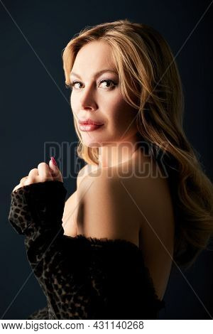 Portrait of a wealthy middle-aged woman with evening makeup and hairstyle posing in black dress on a black background. Luxury lifestyle. Cosmetology, plastic surgery, rejuvenation.