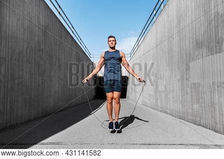 fitness, sport and exercising concept - man skipping with jump rope outdoors