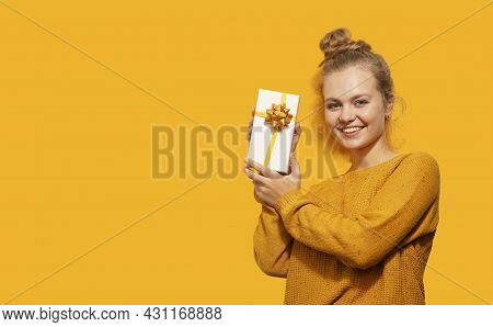 Smiling Beautiful Blonde Young Woman Holding A Gift Box Isolated Over Yellow Background. Happy Birth
