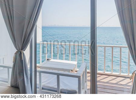 The View From The Interior Of A Room With White Curtains Looking Through The Window Overlooking A Ba