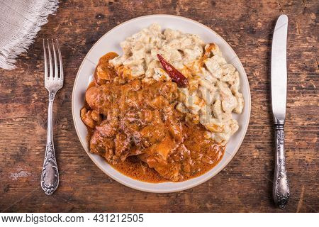 Portion Of Chicken Paprikash With Gnocchi Or Dumplings In A Plate With A Fork And Knife On A Wooden 
