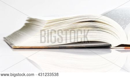 An Open Thick Book Lies On A White Reflective Background. School, College Or University Learning Con