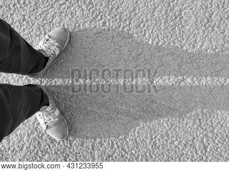 Legs In Sneakers Cast A Shadow On The Asphalt Top View In Black And White