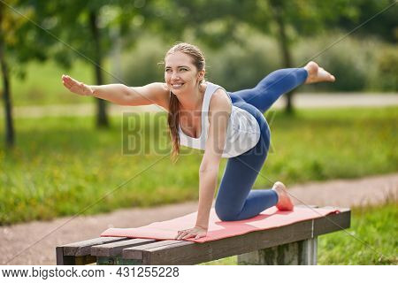 Shoeless Woman Makes Yoga Exercises On Bench In Park.