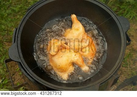 Frying Chicken In Black Cazan With Boiling Oil In Wood-burning Stove On Nature. Two Ruddy Tasty Halv