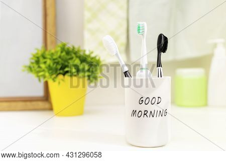 Three Family Toothbrushes Stand In A White Glass On The Bathroom Counter At A Sunny Good Morning. Th