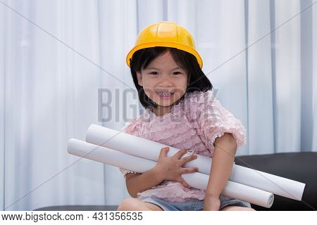 Cute Girl Is Playing The Role Of An Engineer. Asian Child Wears A Yellow Protective Cap And Holds A 