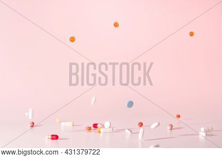 Various colorful pills dropped from above. Medicines jumped on table. Pink background. Selective focus on drugs. Pilules in motion. Close up photo.