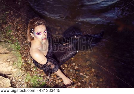 Dark Mermaid Posing Near Sea Shore On Rocks While Wearing Artistic Makeup And Facial Strassses And B