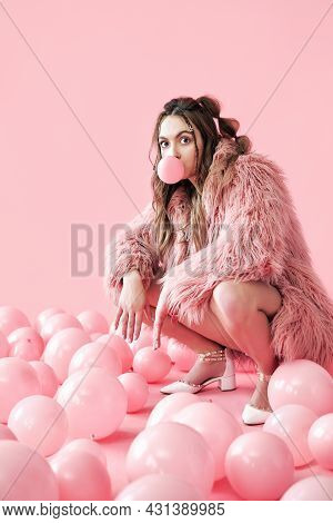 Funny Hipster Woman Blowing Bubble With Chewing Gum Sitting In Pink Balloons Background