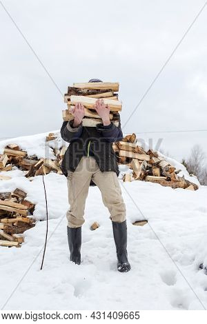 Man Is Carrying An Armload Of Chopped Wood In A Rustic Courtyard, On A Frosty Winter Day. Heating Se