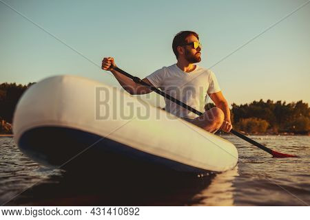 Man Hipster Sits On Paddle Board At Sunset