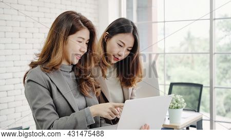 Two Asian Young Creative Businesswomen Holding A Cup Of Coffee, Working On Laptop And Disscuss About