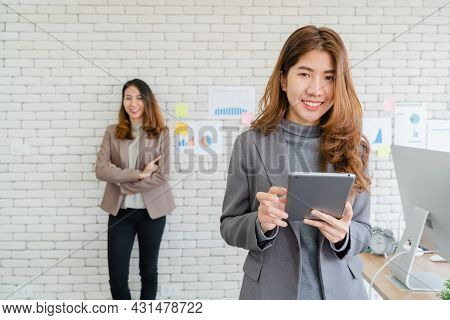 Two Asian Young Creative Businesswomen Holding A Cup Of Coffee, Working On Laptop And Disscuss About