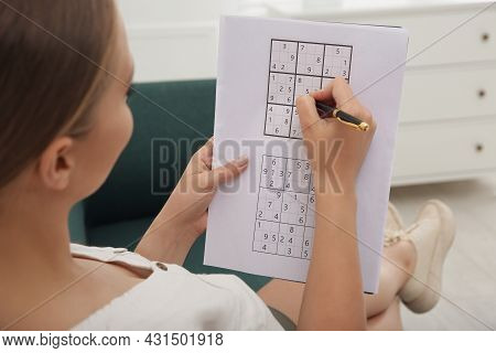 Young Woman Solving Sudoku Puzzle On Sofa Indoors, Closeup