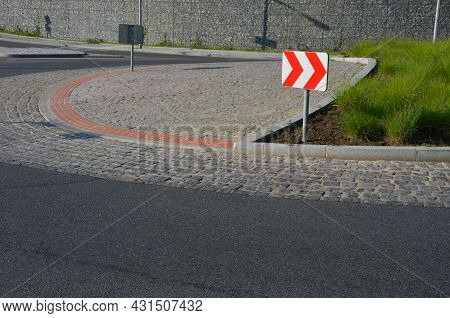 Roundabout Of Gray Granite Cubes Closer To The Center. Beveled Concrete Curbs With Flowers And Grass