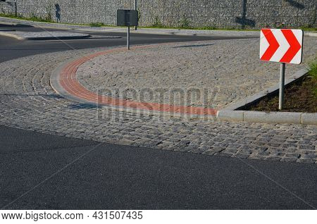 Roundabout Of Gray Granite Cubes Closer To The Center. Beveled Concrete Curbs With Flowers And Grass