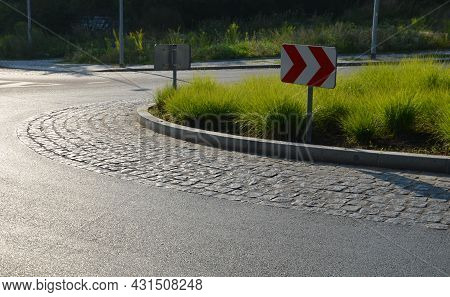 Roundabout Of Gray Granite Cubes Closer To The Center. Beveled Concrete Curbs With Flowers And Grass