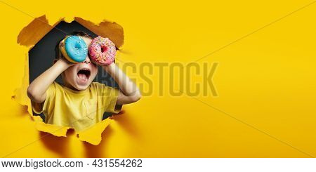 Happy cute boy is having fun played with donuts on Yellow background wall. Bright photo of a boy. Colored donuts