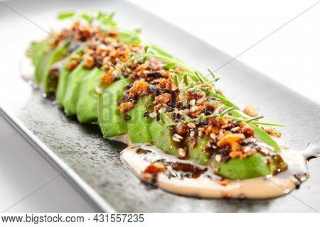 Avocado carpaccio green salad on white background. Healthy organic vegan food. Ketogenic diet. Appetizers avocado slices with unagi sauce and peanut. Trend dish in restaurant menu