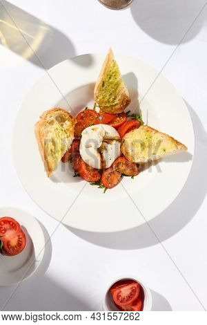 Traditional Italian salad with Burrata cheese and tomatoes. Fancy caprese with burrata cheese, cherry tomatoes, pesto and balsamic sauces. Summer dish with mozzarella cheese on white table with shadow