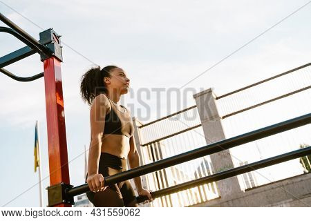 Concentarted young fit african fitness woman exercising on parallel bars at the sportsground