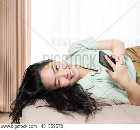 Beautiful Asian Woman Is Lying Down And Playing Mobile On The Bed In Her Bedroom With A Pastel Green