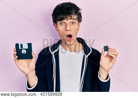Handsome hipster young man holding floppy disk and sdxc card afraid and shocked with surprise and amazed expression, fear and excited face. 