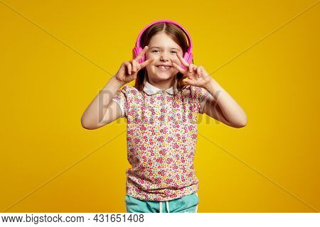Lovely Kid In Summer Clothes, Listens Audio Track In Pink Headphones, Makes Peace Gesture, Isolated 