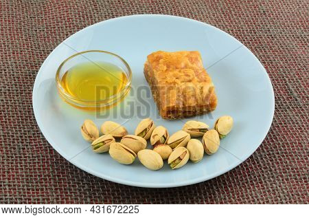 Piece Of Baklava With Honey In Glass Bowl And Pistachio Nuts In Shells On Blue Snack Plate