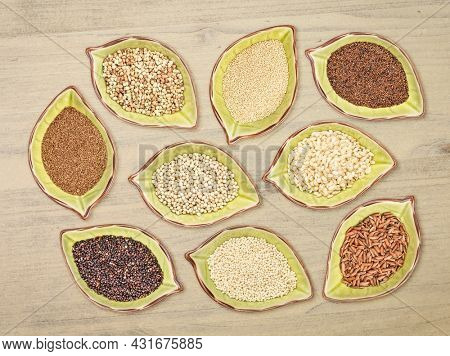nine gluten free grains (black quinoa, buckwheat, amaranth, teff, sorghum, kaniwa, millet, and brown rice) - top view of leaf shaped ceramic bowls against distressed wood