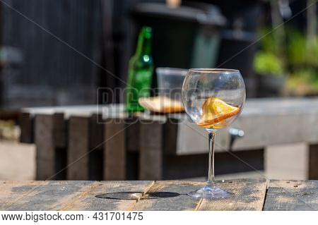 Empty Wine Glass On Wooden Table, Background Blurred Empty Green Bottle And Plastic Cup On Rustic Ta