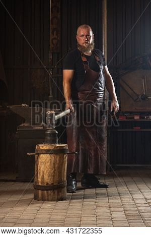 Full Ength Portrait Of Bearded Man, Blacksmith Working On Creating Handmade Metal Product At Family 