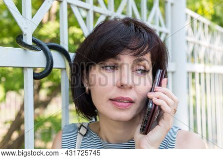 A Woman Is Talking On The Phone On The Street By The Fence Not Noticing A Poisonous Snake Near Her H