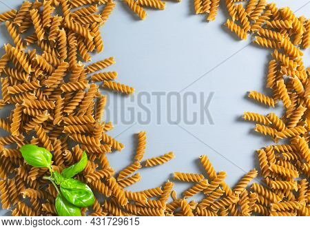 Raw Fusilli Pasta With A Sprig Of Green Basal On A Gray Background. Whole Grain Pasta. Top View. Hea