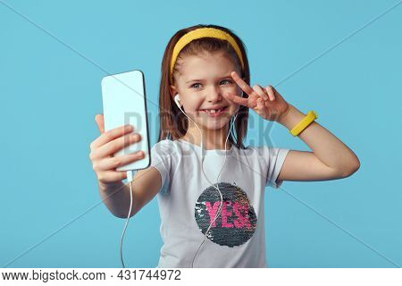 Photo Of Carefree Kid Takes Selfie Portrait On Mobile Phone, Shows Peace Gesture, Wears White T Shir