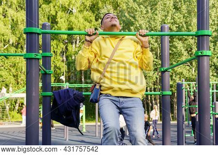 A Young Man In A Yellow Jacket Pulls Himself Up On A Horizontal Bar. Selective Focus. Sports Event