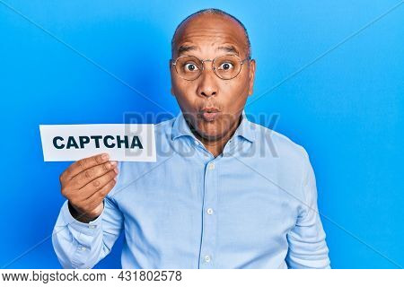 Middle age latin man holding captcha message paper scared and amazed with open mouth for surprise, disbelief face 