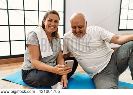 Middle age hispanic couple using smartphone at sport center.