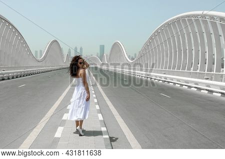 A Woman In A White Sundress Walking On An Empty Road Toward To The City, Meydan Bridge In Dubai