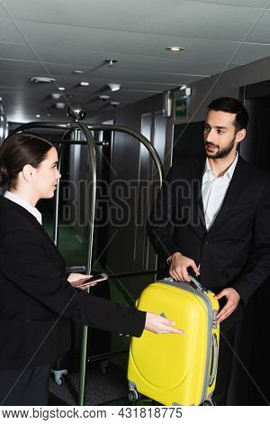 Blurred Receptionist Holding Smartphone And Pointing Near Bellboy With Luggage