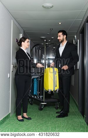 Smiling Receptionist Pointing With Hand Near Bellboy With Luggage