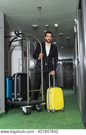 Full Length Of Bearded Bellboy Near Metallic Bell Cart With Luggage In Hall Of Hotel