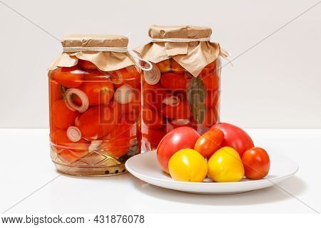 Tomatoes Preserved In Glass Jars And Fresh Tomatoes On A Plate. Pickled Tomatoes On The White Backgr