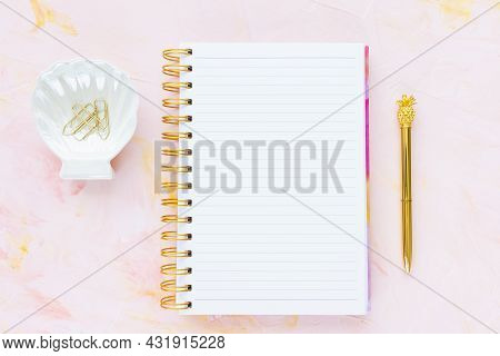Open Notepad, Gold Pen, White Seashell Decoration With Paper Clips On Woman Desk Workspace, Pink Bac