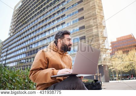 Young Businessman Works With Laptop Outdoors. Entrepreneur In Casual Clothes In A Corporate Area. Ma