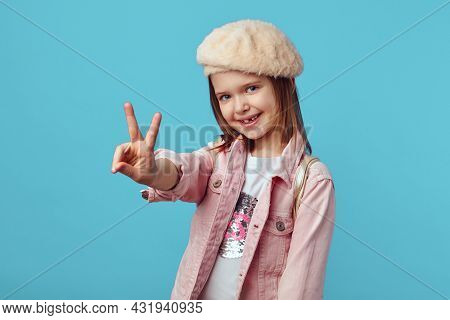 Attractive Caucasian Girl In Pink Jacket And Hat Smiling And Showing Peace Gesture Against Blue Stud