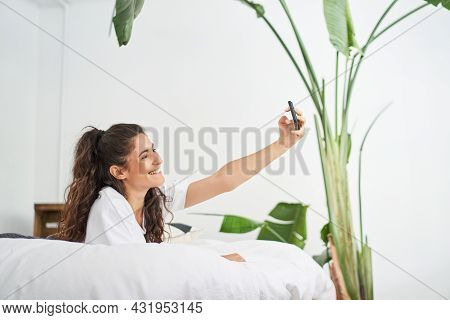 Pretty Young Latina Woman Takes A Selfie Lying On The Bed. Influencer Sharing On Social Networks And