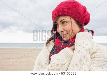 Close up of a young woman in knitted hat and pullover looking away on the beach