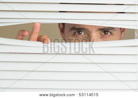 Focused beautiful brown male eyes spying through roller blind